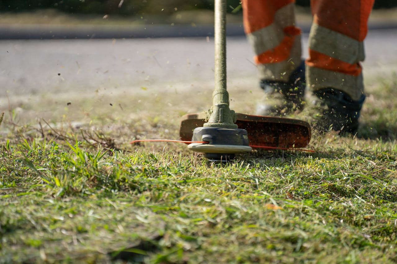 services-02 Close-up of a person trimming grass with a power tool outdoors.
