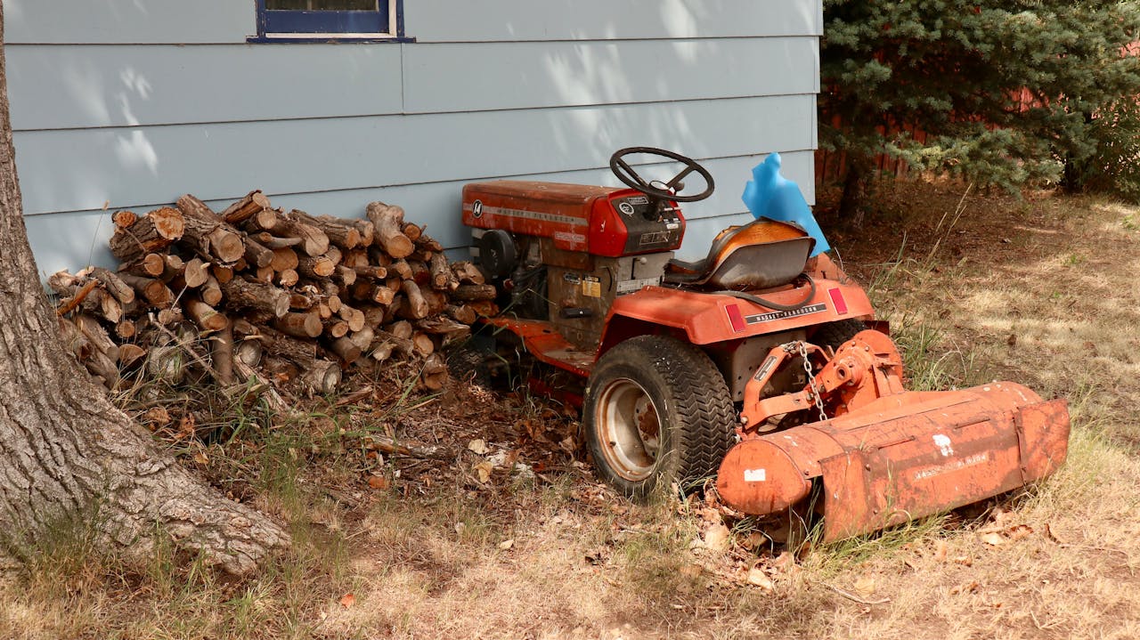 services-01 An old red tractor beside a stack of firewood outdoors.
