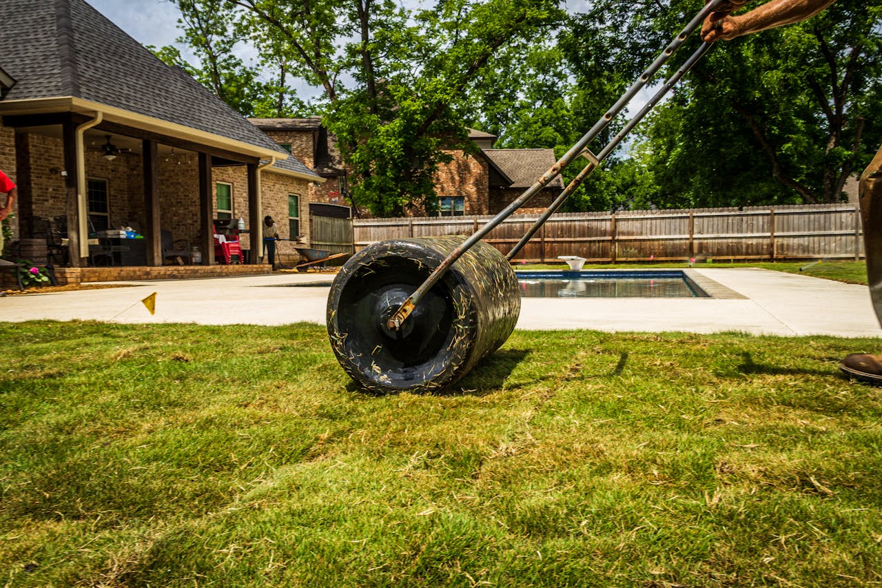 services-03 A worker rolling a lawn in a suburban backyard near a pool on a sunny day.